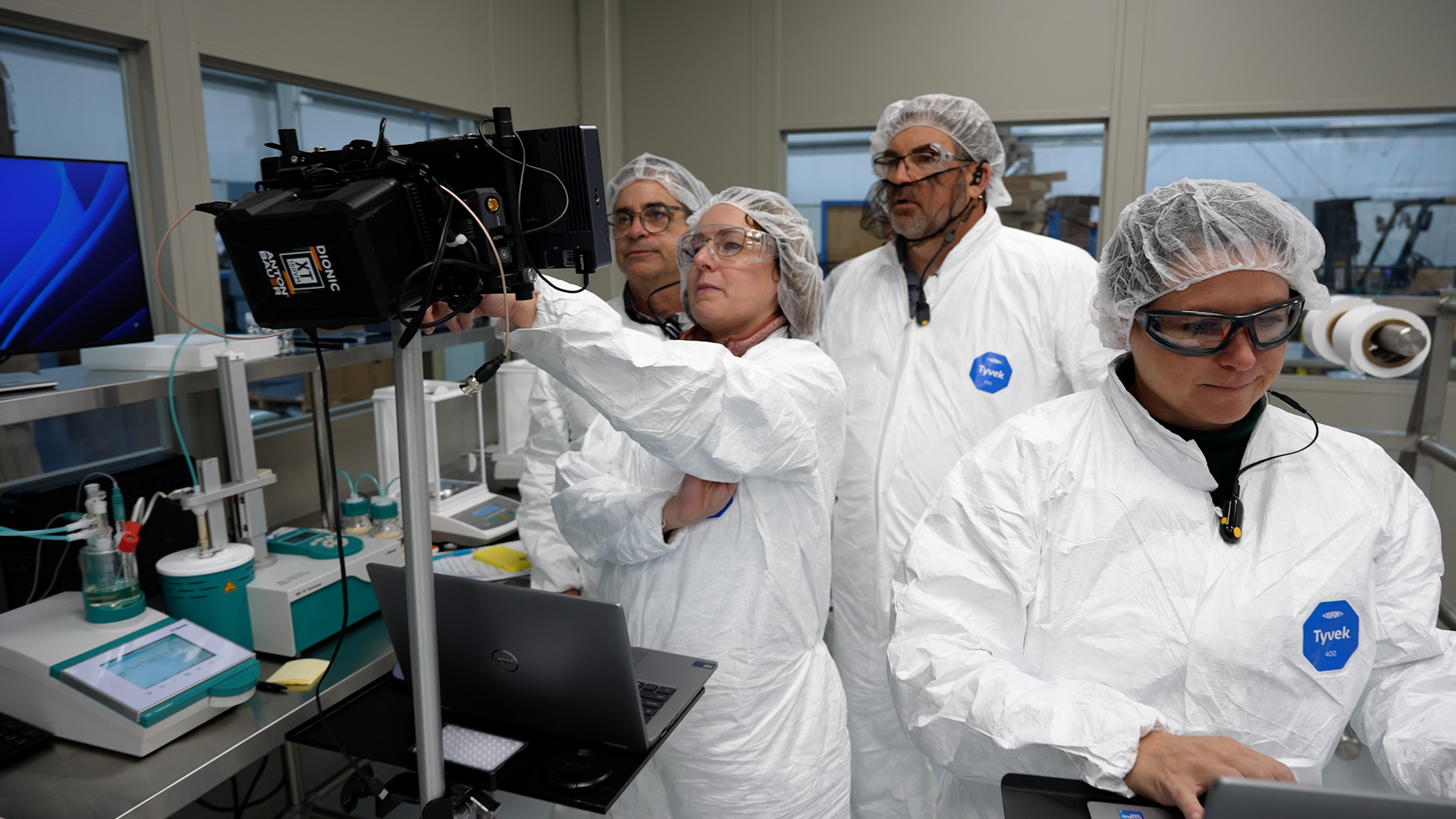 Photo of 4 employees in lab coats looking at a monitor
