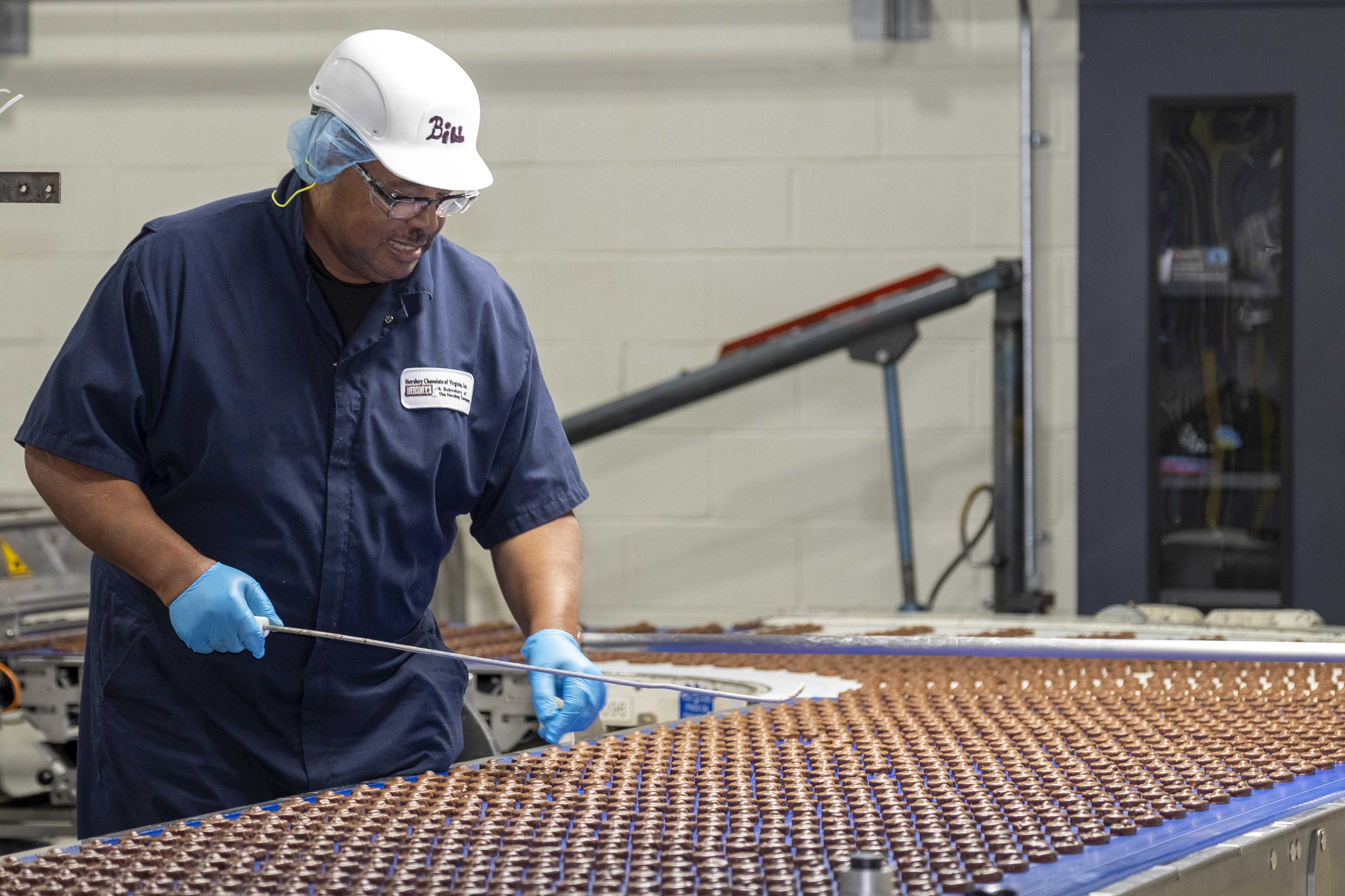 A man wearing safety equipment and inspecting chocolates on a conveyor belt