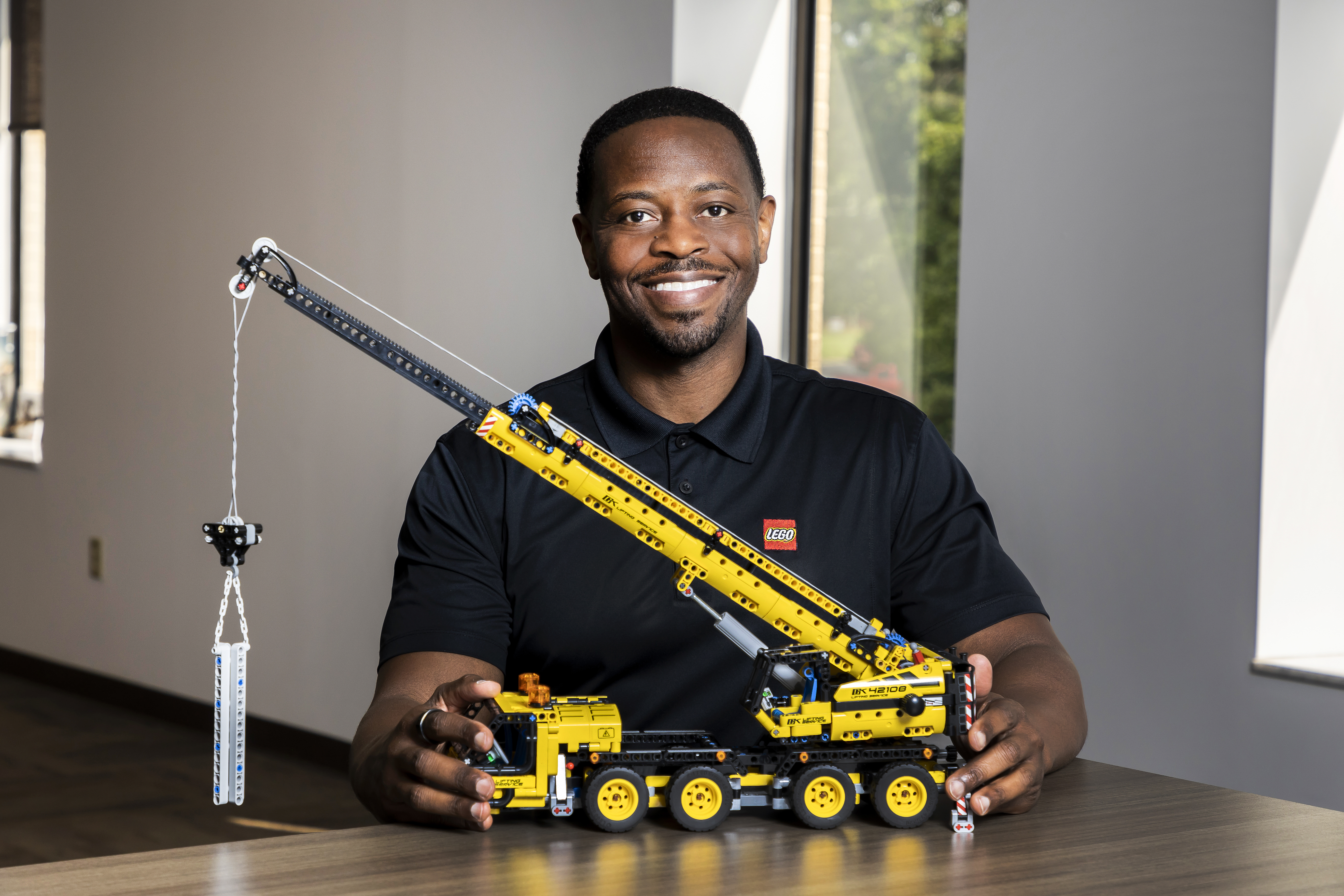A smiling man holding a truck made with LEGO blocks
