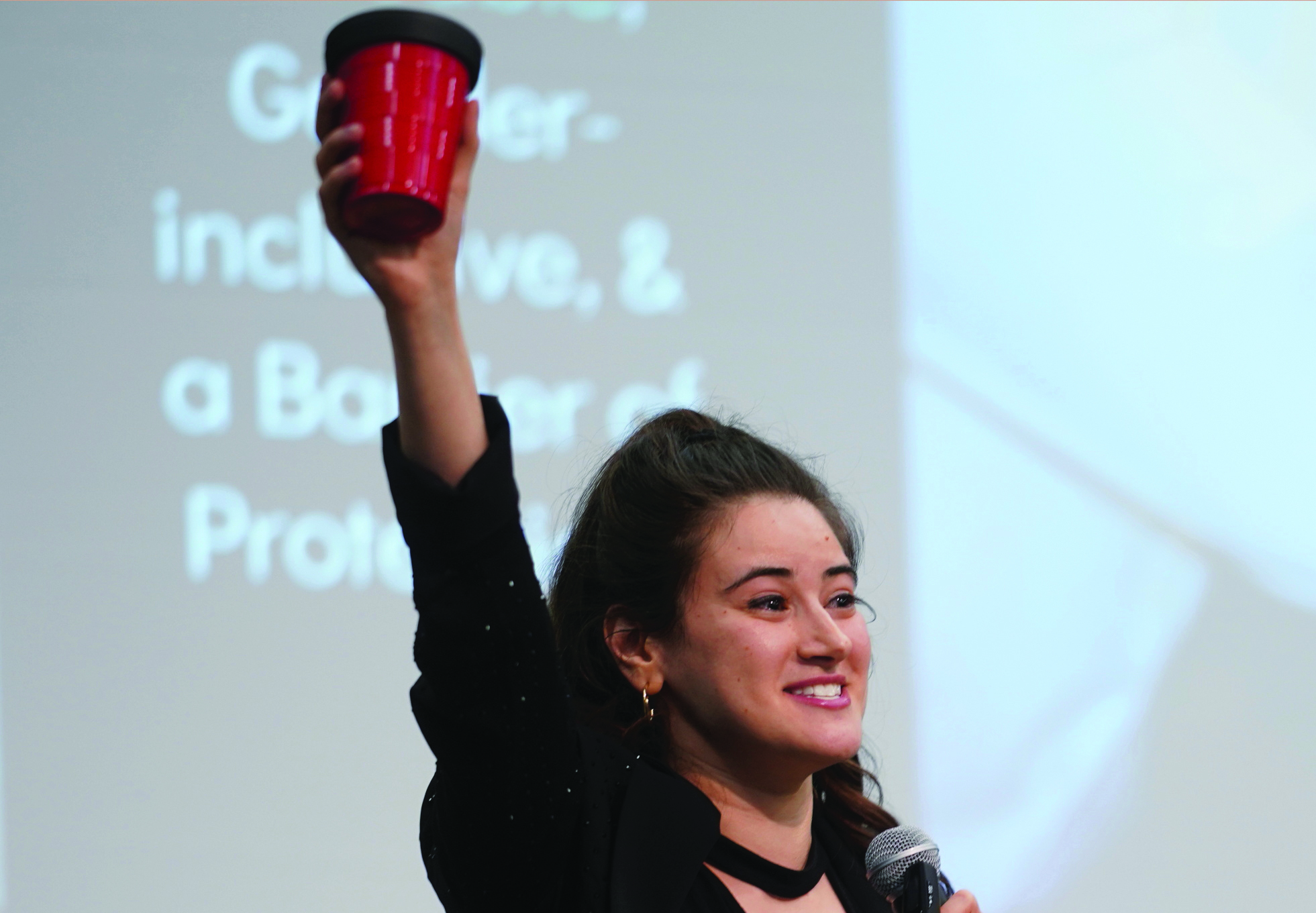 Women standing in front of a screen holding up a red cup