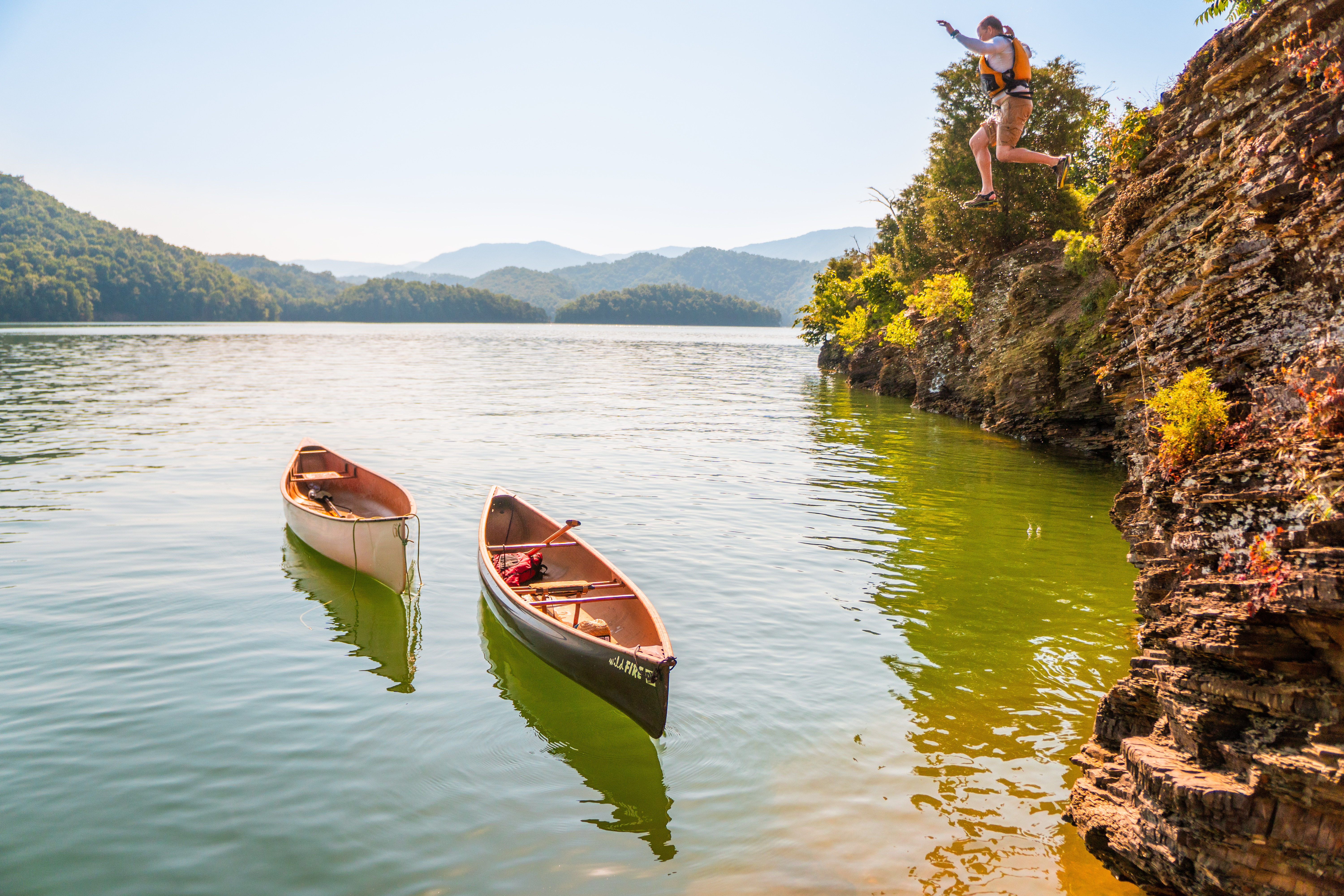 People cliff jumping over kayas