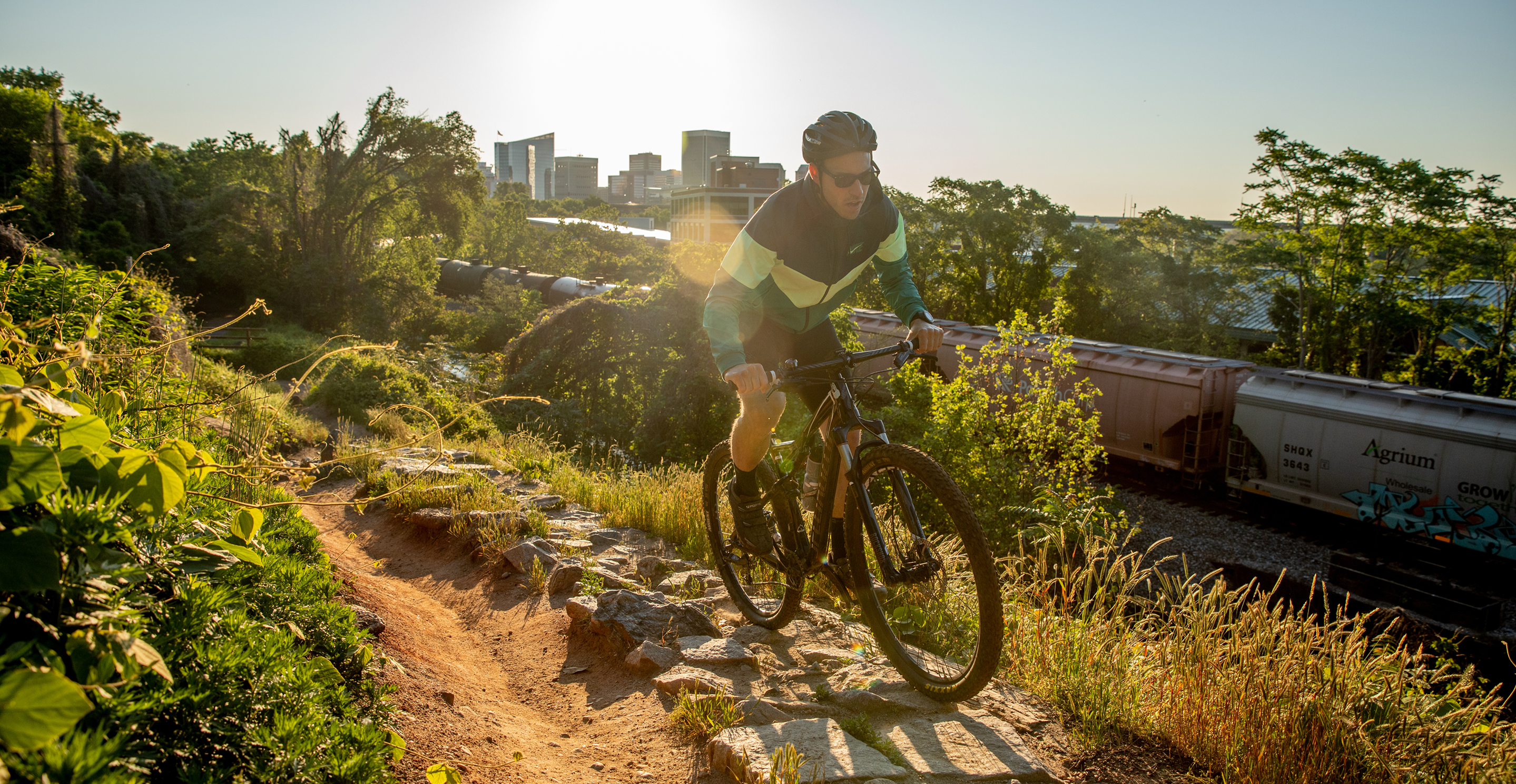 Man on a mountain bike riding a trail with a city skyline in the background