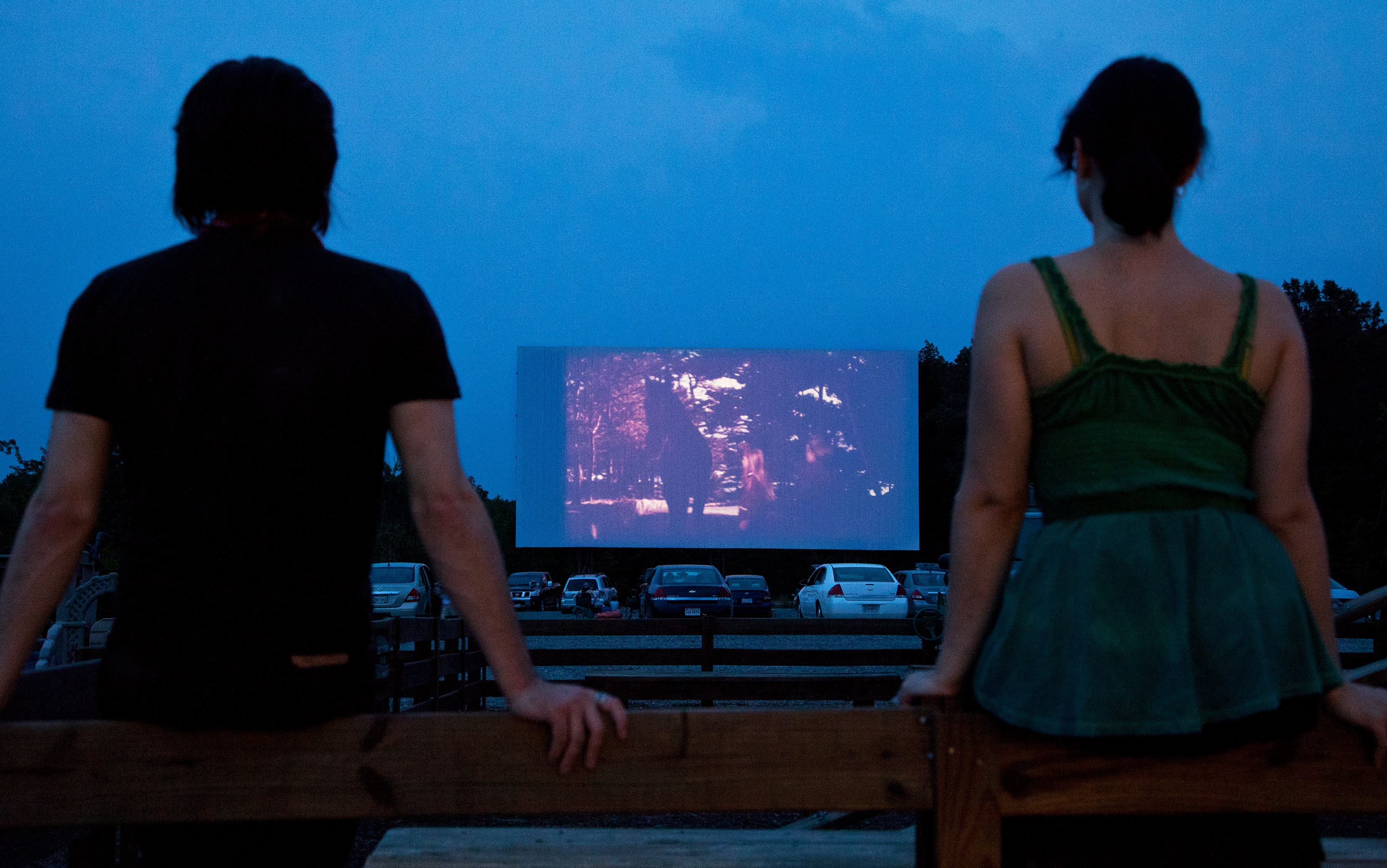 Two people watching movie at drive-in theatre.
