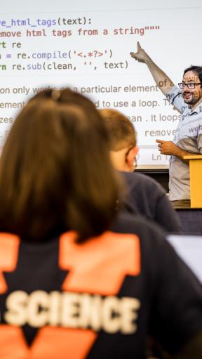 A man teaching a class and pointing to computer code